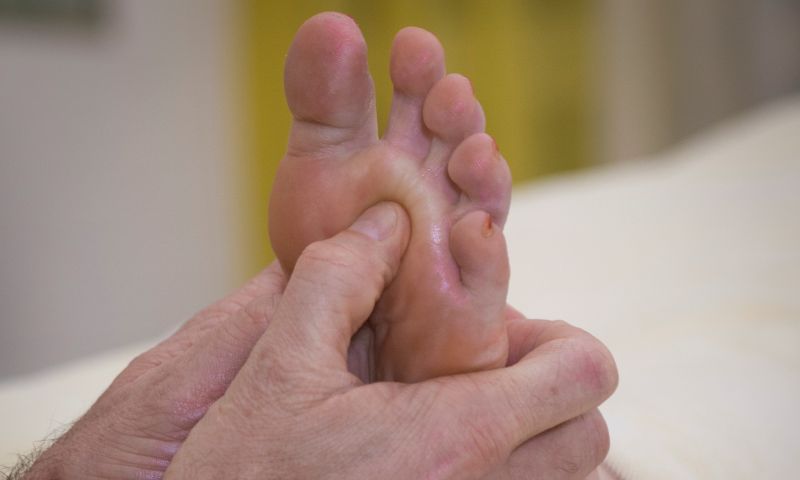 Beide Hände behandeln die Reflexzonen am Fuss einer liegenden Person