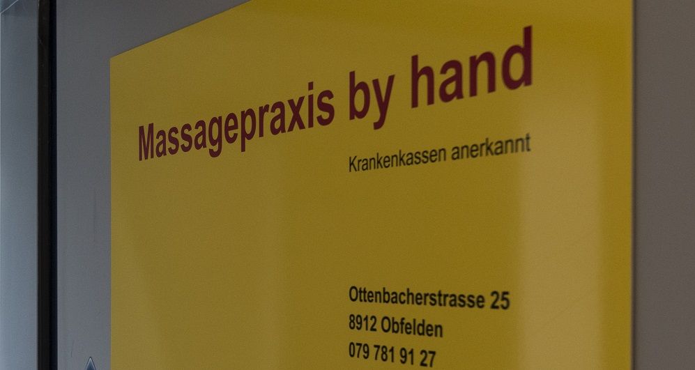 Gelbes Praxisschild «Massagepraxis by hand – Krankenkassen anerkannt»